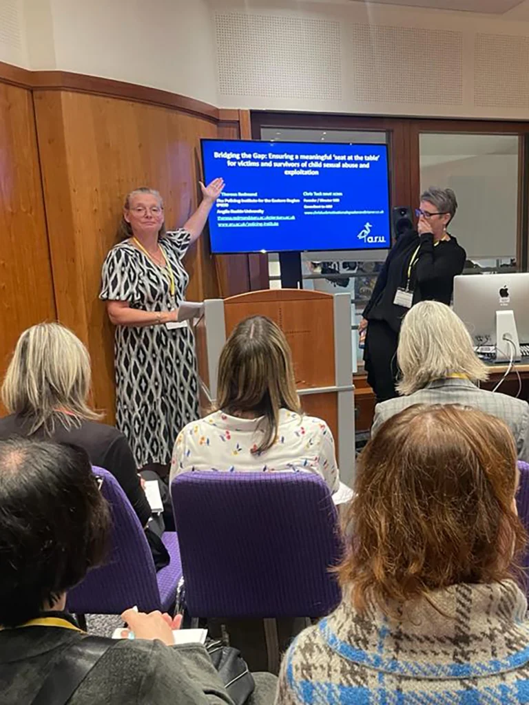Speaker Chris Tuck standing next to a TV screen delivering a speech as a motivational speaker